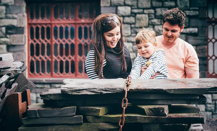Parents and young son look at a pile of dressed slates piled onto a wagon in the workshop yard.